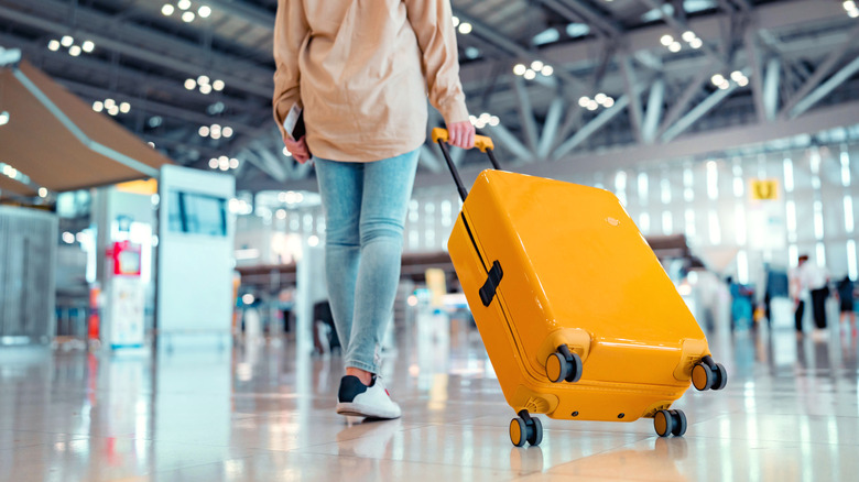 Young female traveler passenger walking with a yellow suitcase in a modern Airport Terminal