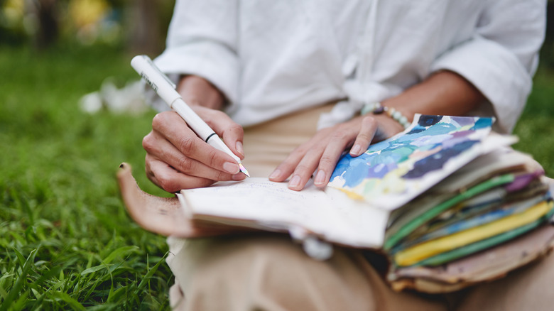 Woman outside writing in artistic notebook