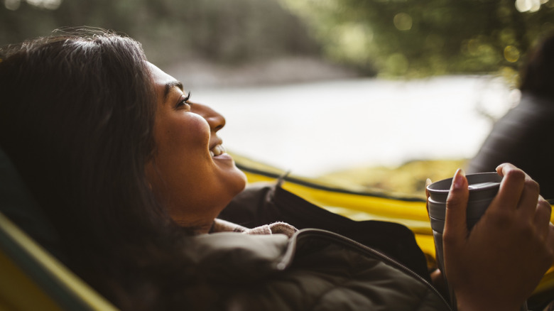 Woman relaxing in hammock by lake with mug in hand