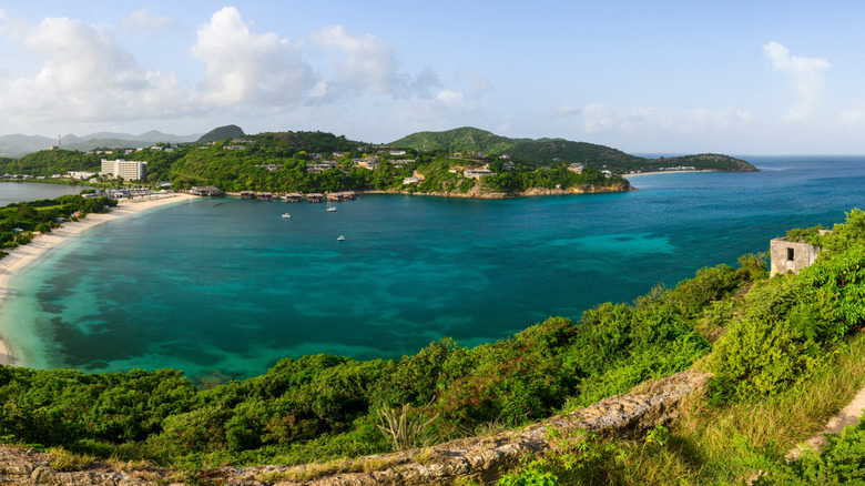 A narrow, white, sandy beach in Deep Bay, Antigua, with a multi-story hotel in the background