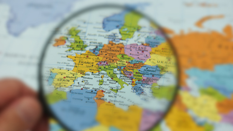 A hand holds a magnifying glass over a colorful map of Europe,