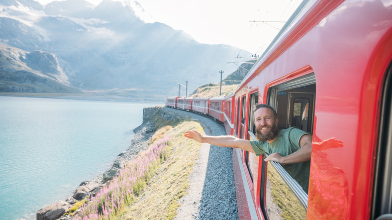 A passenger enjoying a scenic train journey along a lakeside mountain route.