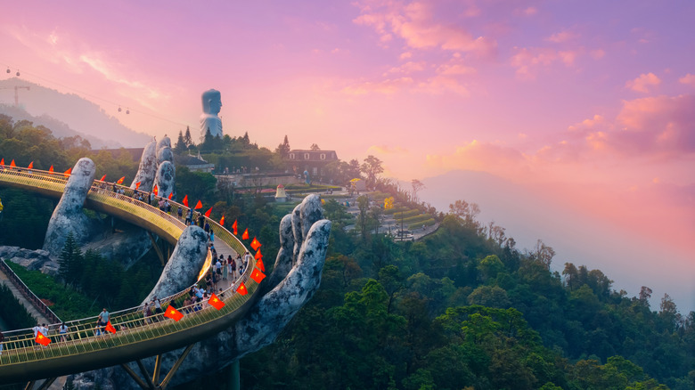 Bridge held up by stone hands in the ba na hills against a pink sky at sunset.