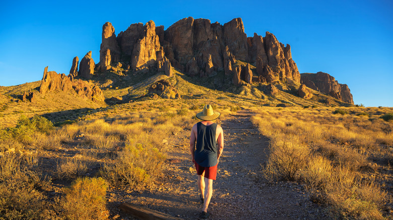 A hiker in a straw hat walks up a path in Arizona's Superstition Mountains
