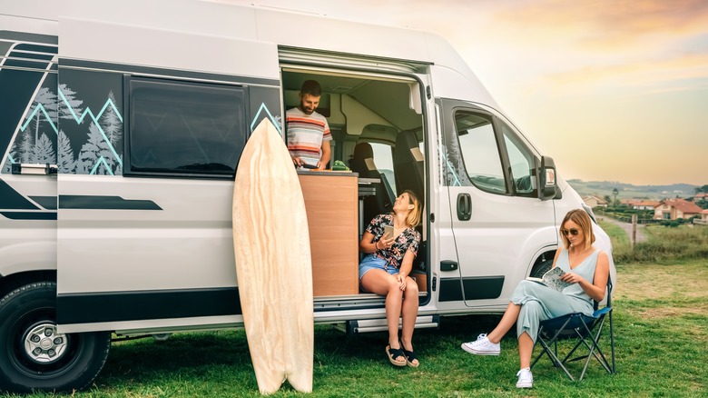 Friends sitting around a camper with a surfboard