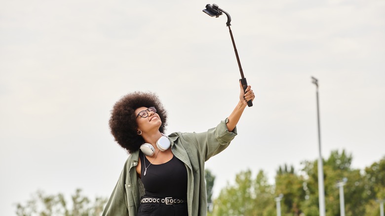 A woman uses a selfie stick to take a self-portrait outside