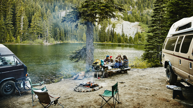 Family and friends sharing a meal together at campsite by lake in mountains🔍🔍🔍