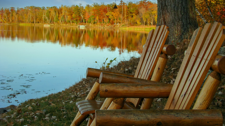 wooden chairs on lake shore, fall foliage in background