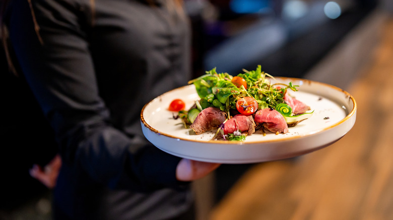 Person holding a plate of gourmet salad with seared tuna