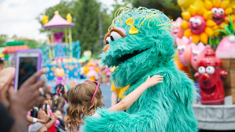 A child hugging a Sesame Street character at a theme park.