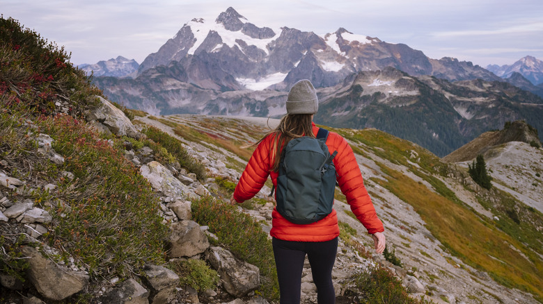 A woman in a puffer jacket and backpack climbing a mountain.