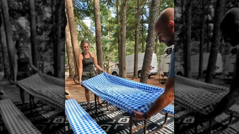 A couple putting their blue checkered picnic table cover on a table