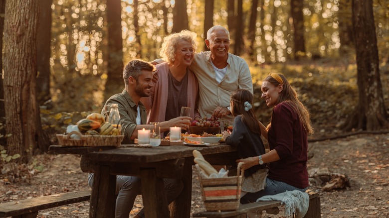 A family enjoying a meal at a picnic table in the woods