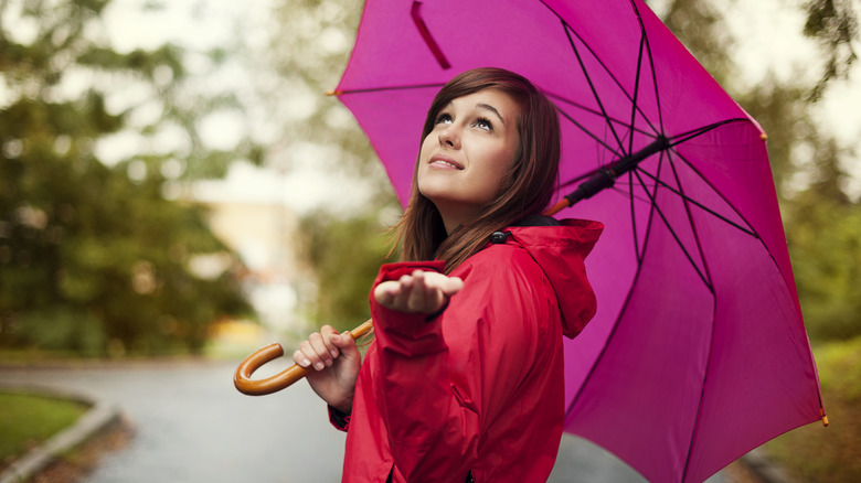 A woman with an umbrella holds her hand out while looking up at the sky.