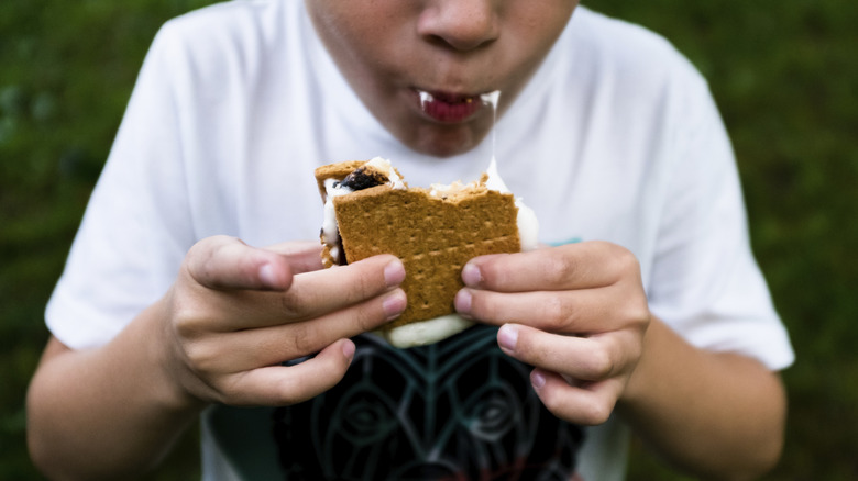 A young person takes a bite out of a s'more.