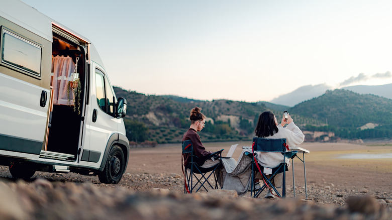 couple sitting in chairs next to camper van with mountain background
