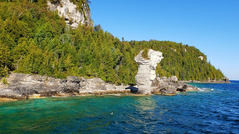 An image of turquoise waters and greenery with a tall rock formation along the shoreline