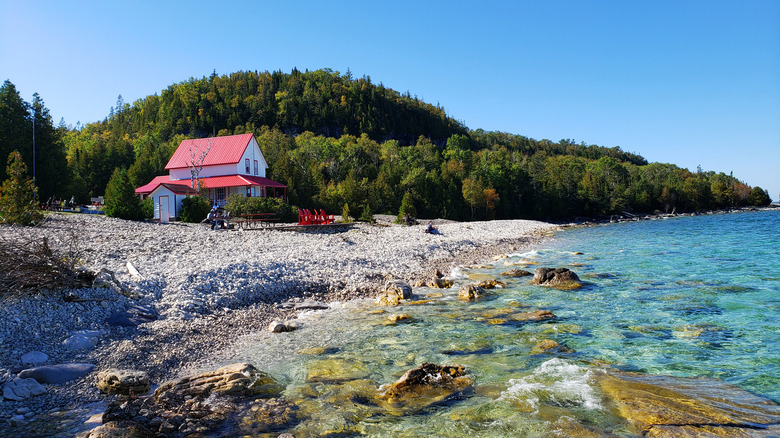A rocky beach with turquoise waters and a red roofed building