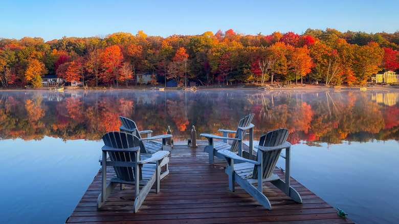 Mist on a lake with four chairs on a dock with colorful autumn trees