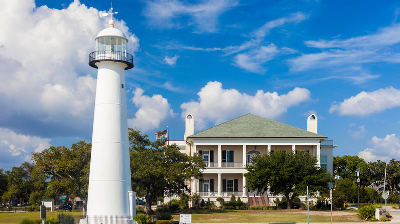 A two-story building surrounded by trees with a lighthouse in the forefront.