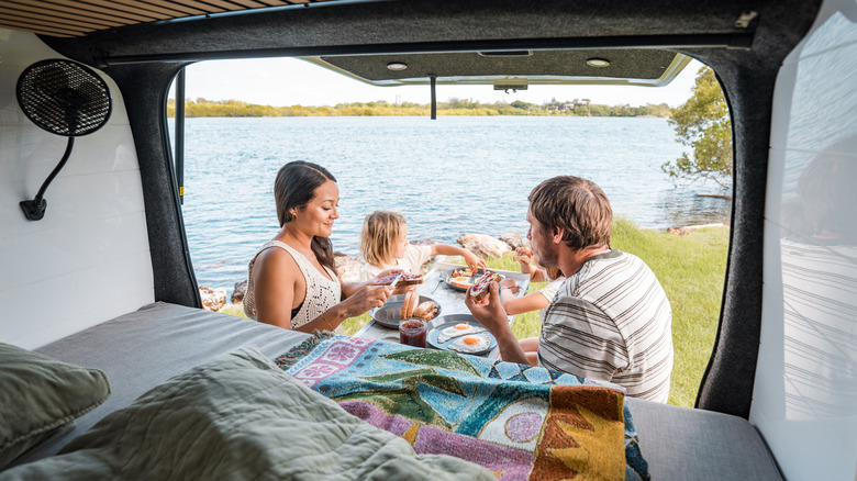 Family having breakfast lakeside with campervan