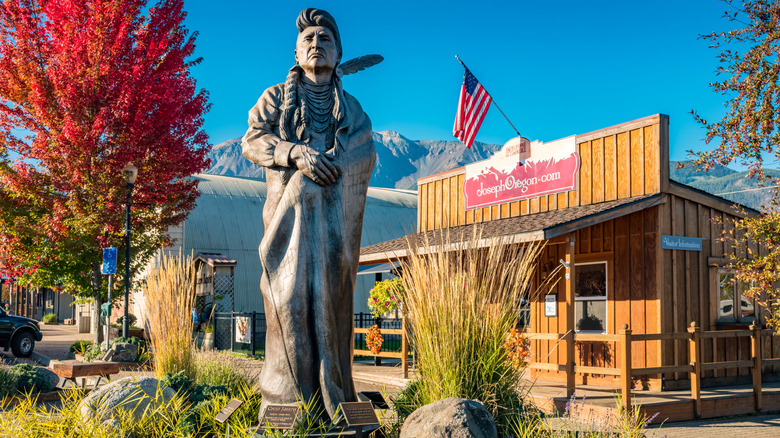 statue of indigenous man, trees, wooden building