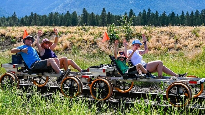 tourists waving on railroad pedal carts, grass and trees
