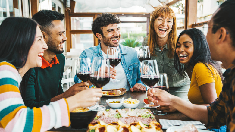 A group of friends around a table laughing and holding glasses of wine