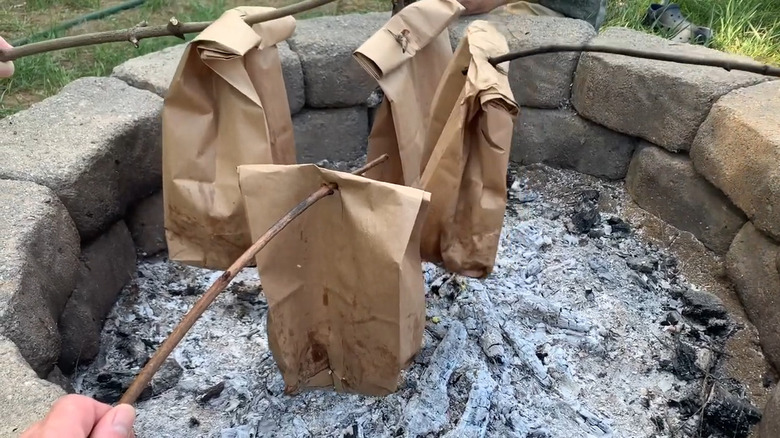 Four paper bags on sticks over coals.