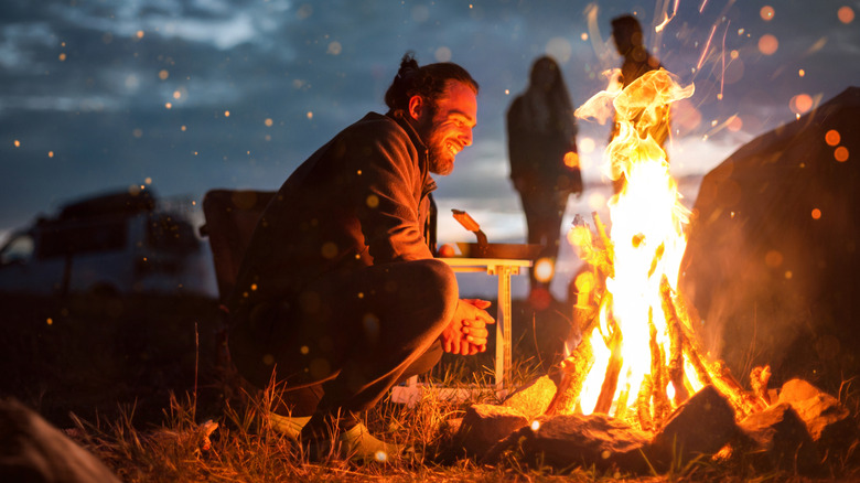A man crouching by a campfire.
