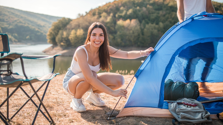 Smiling woman crouching down beside a blue tent