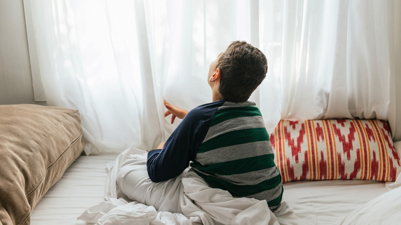 A child sits on a bed behind a wall of curtains.
