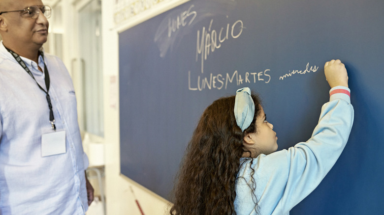 A young girl writes the Spanish name for days of the week on a chalkboard