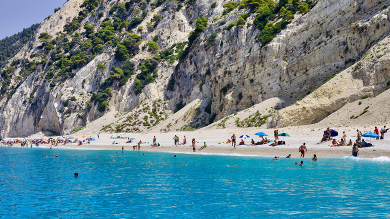 A white sand beach with a cliff and blue water with people on the beach
