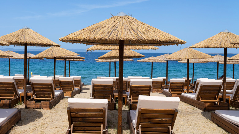 Rows of beach lounge chairs with seas view with thatched umbrellas