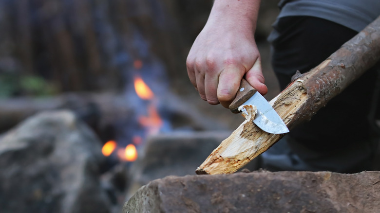 A man carves a piece of wood with a camping knife