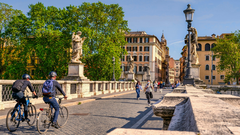 two people on bikes crossing a bridge in rome