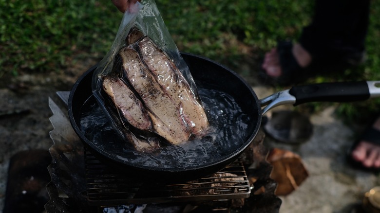 hand putting vacuum-sealed meat into skillet with water can campsite