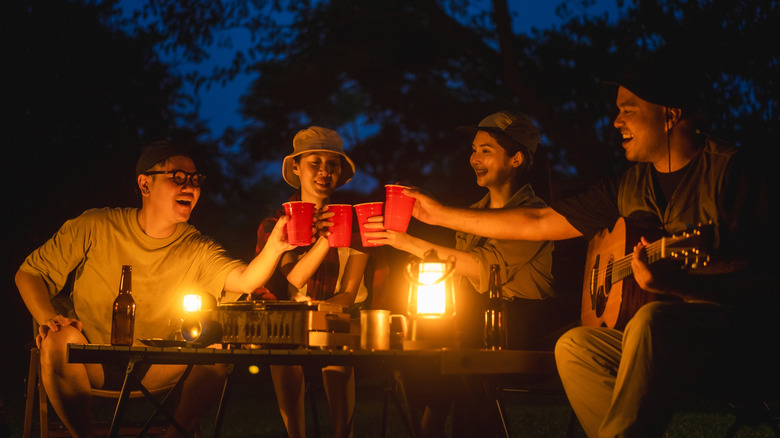 Friends toast with red cups around a campsite's picnic table at night