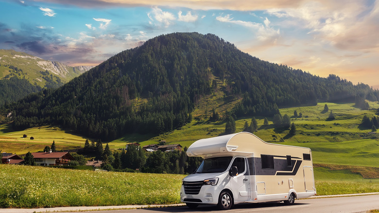 An RV camper on the road in front of a mountain.