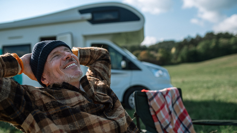 A man relaxes and smiles in front of his RV.