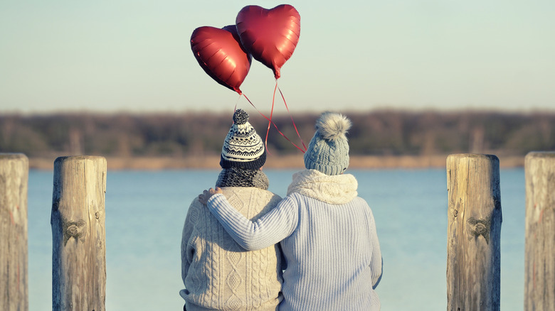couple holding heart balloons near winter lake
