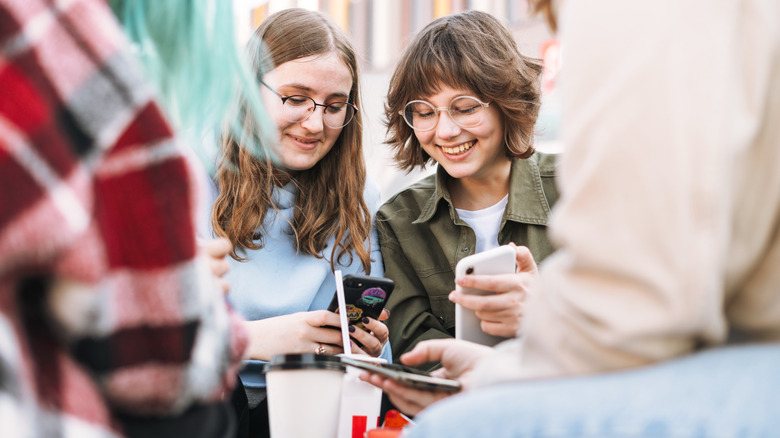 group of teenage girls smiling while using their mobile phone