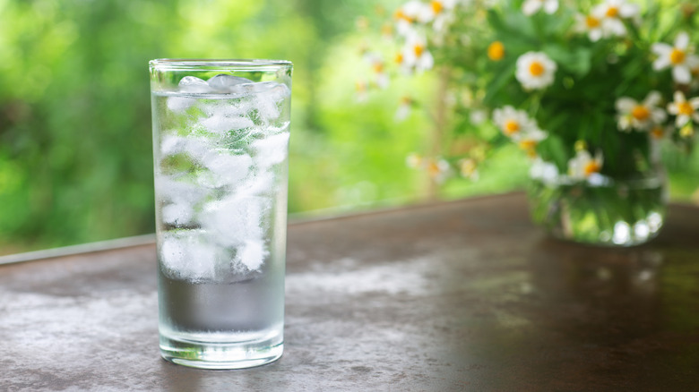 A glass of ice water stands near flowers.