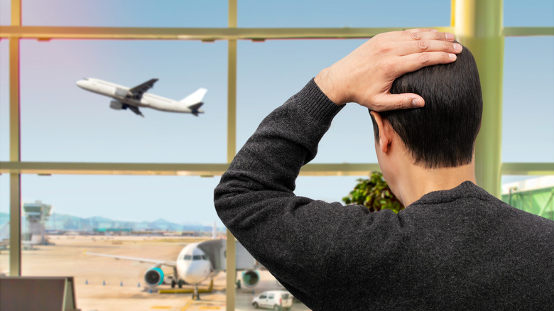 An unhappy man watches a plane take off at an airport.
