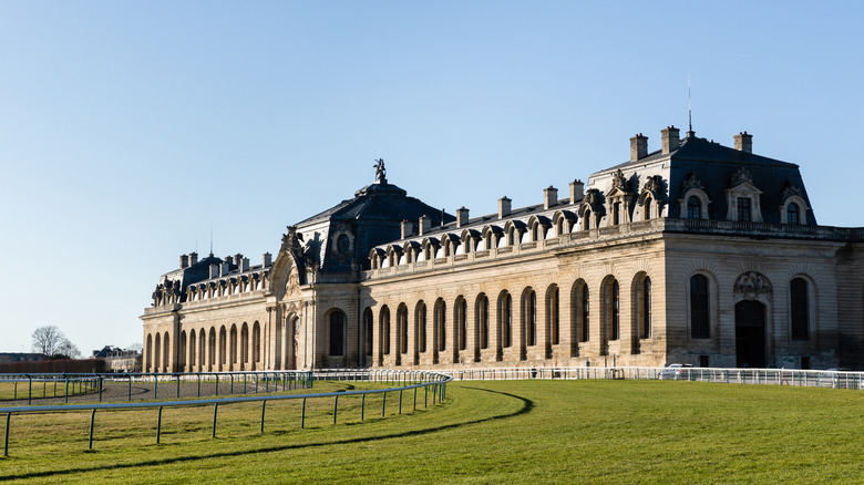 the arched facade of the stables at the chateau de Chantilly with the racecourse in the foreground