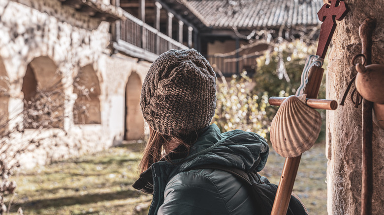 A rear closeup of the back of a woman's head wearing a hat and coat in a small Spanish village