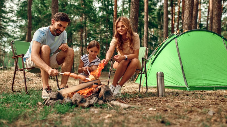 Happy family roasting food over a campsite fire