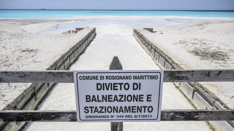 A warning sign in Italian over a canal with white flowing liquid