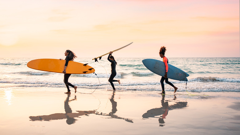 Three people by the sea holding surfboards